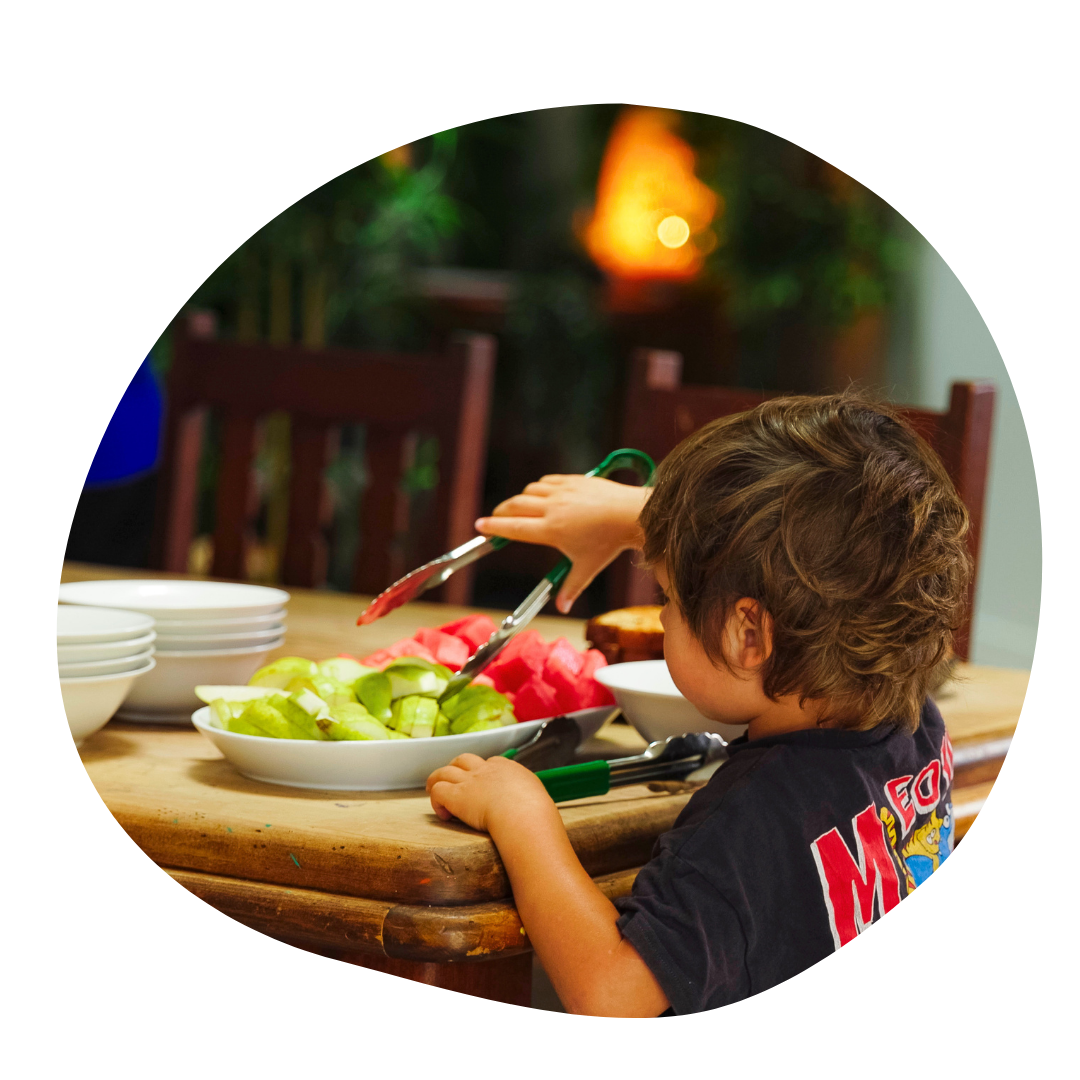 Young child using kitchen tongs to serve fruit onto their own plate