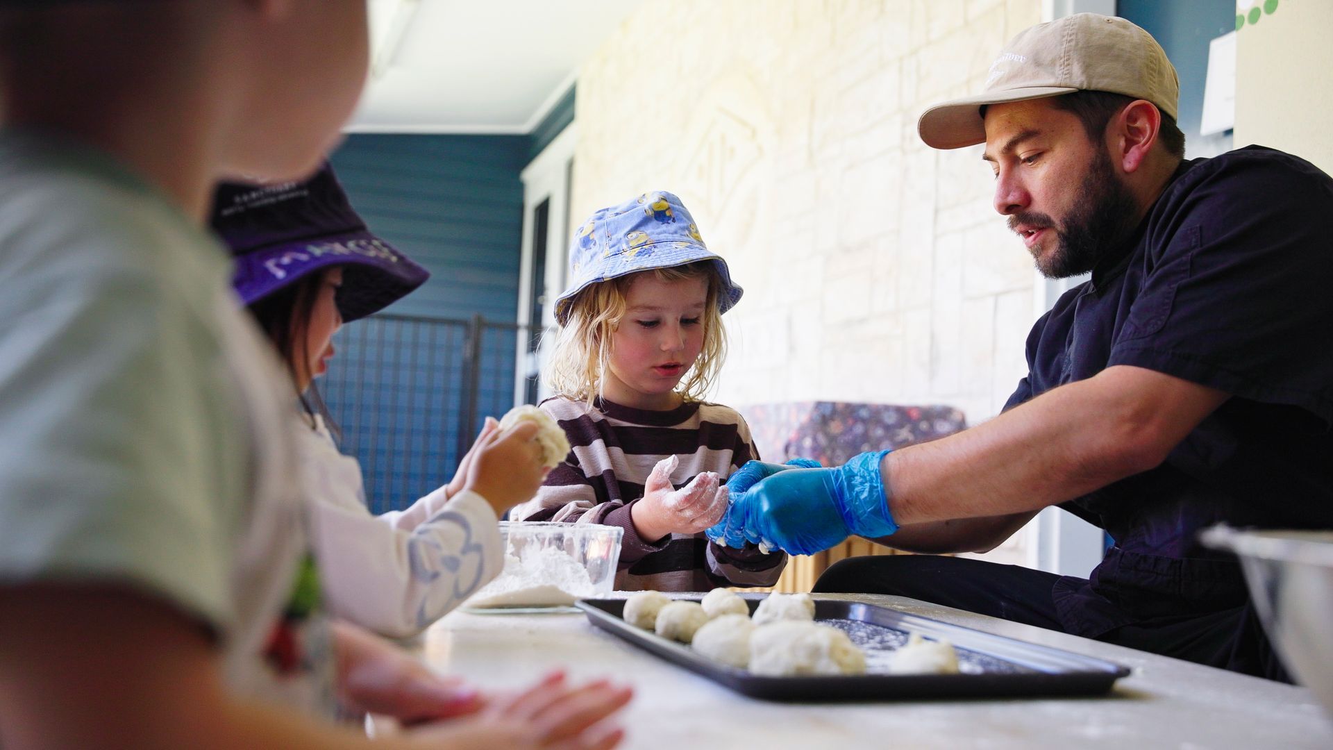 Children sit at a table and make food with a cook