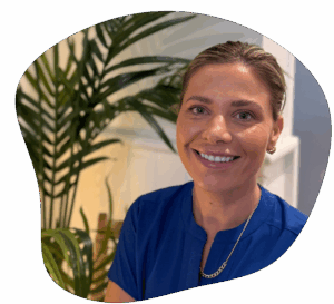 Woman in blue shirt smiles, with leafy plant in background.