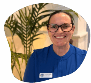 Woman with glasses smiles, wearing a blue shirt. Name tag reads 