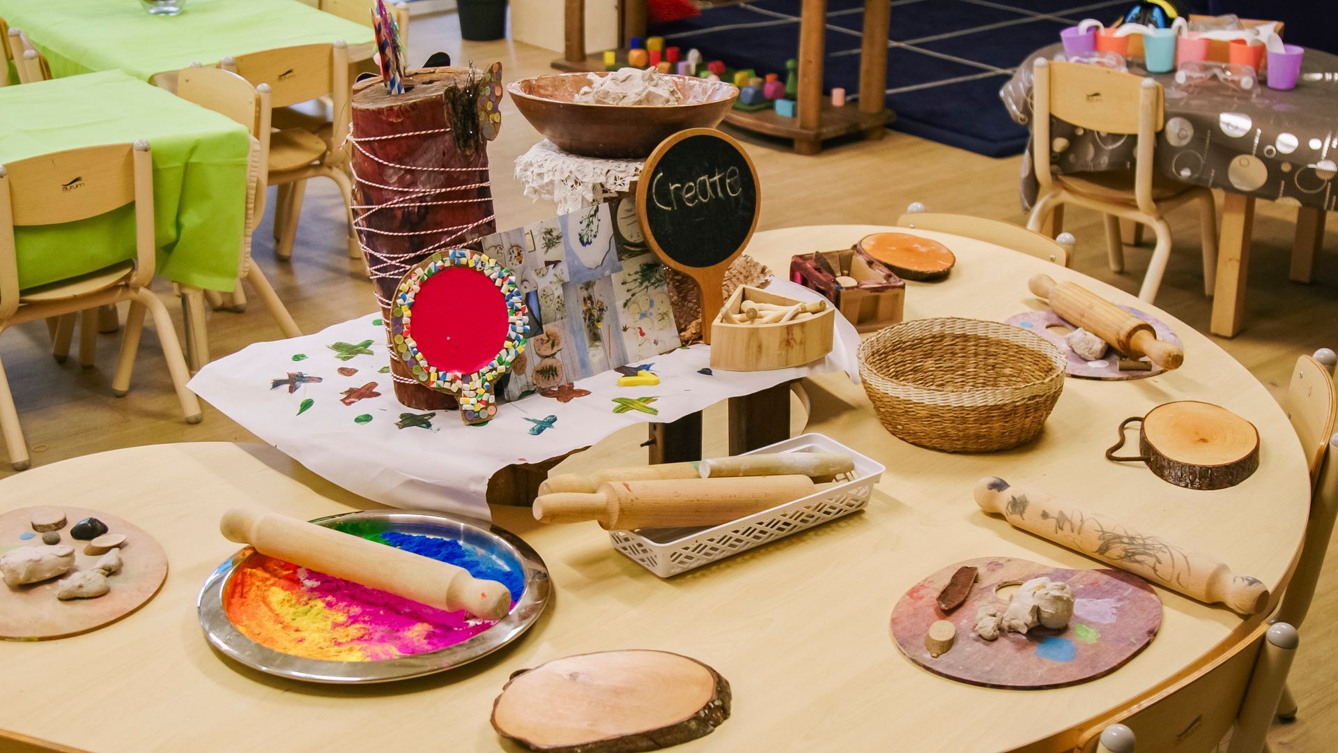 Child-sized wooden tables with art supplies like rolling pins, paints, and wood slices are set up for crafting.