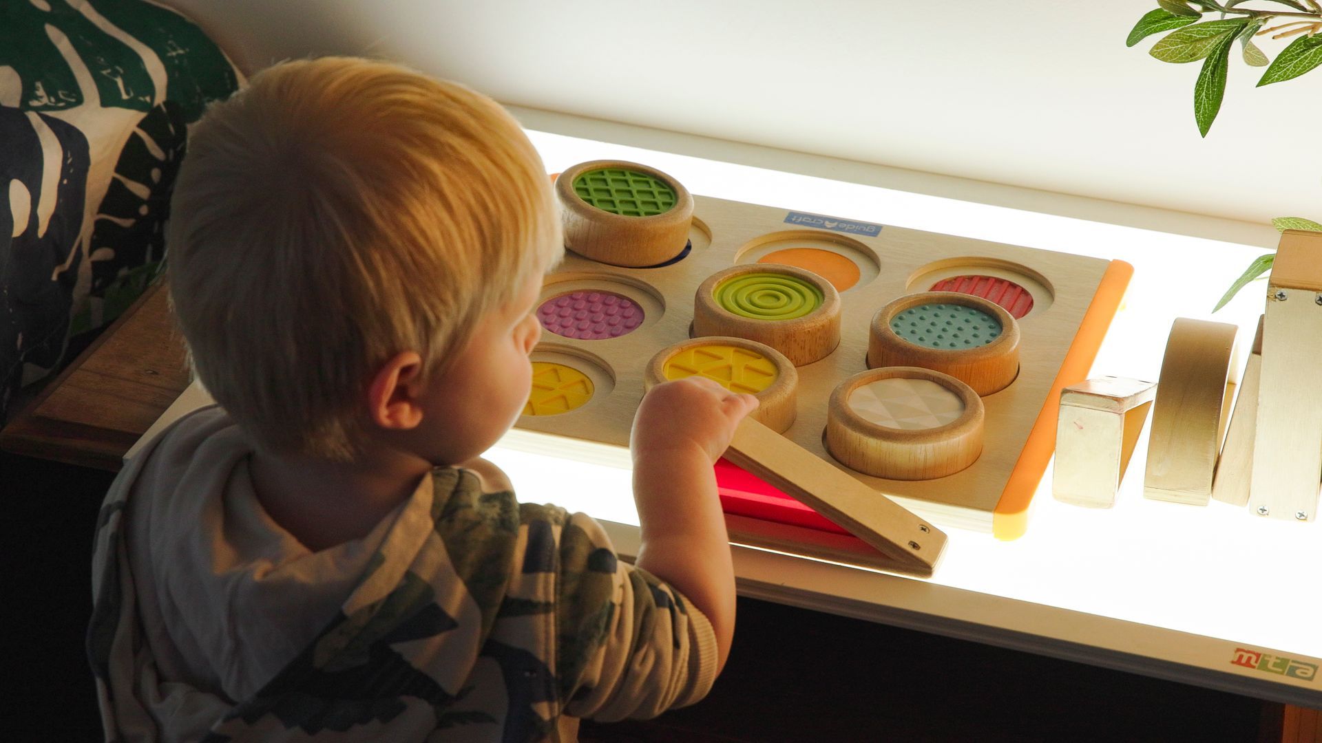 Young child inside looking at colourful shapes with light shining upward