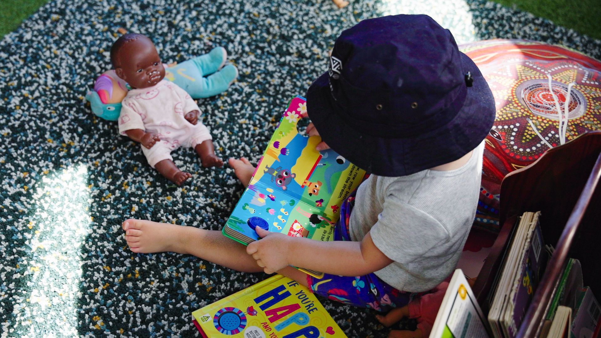 young child sitting and reading book on the floor with a hat on