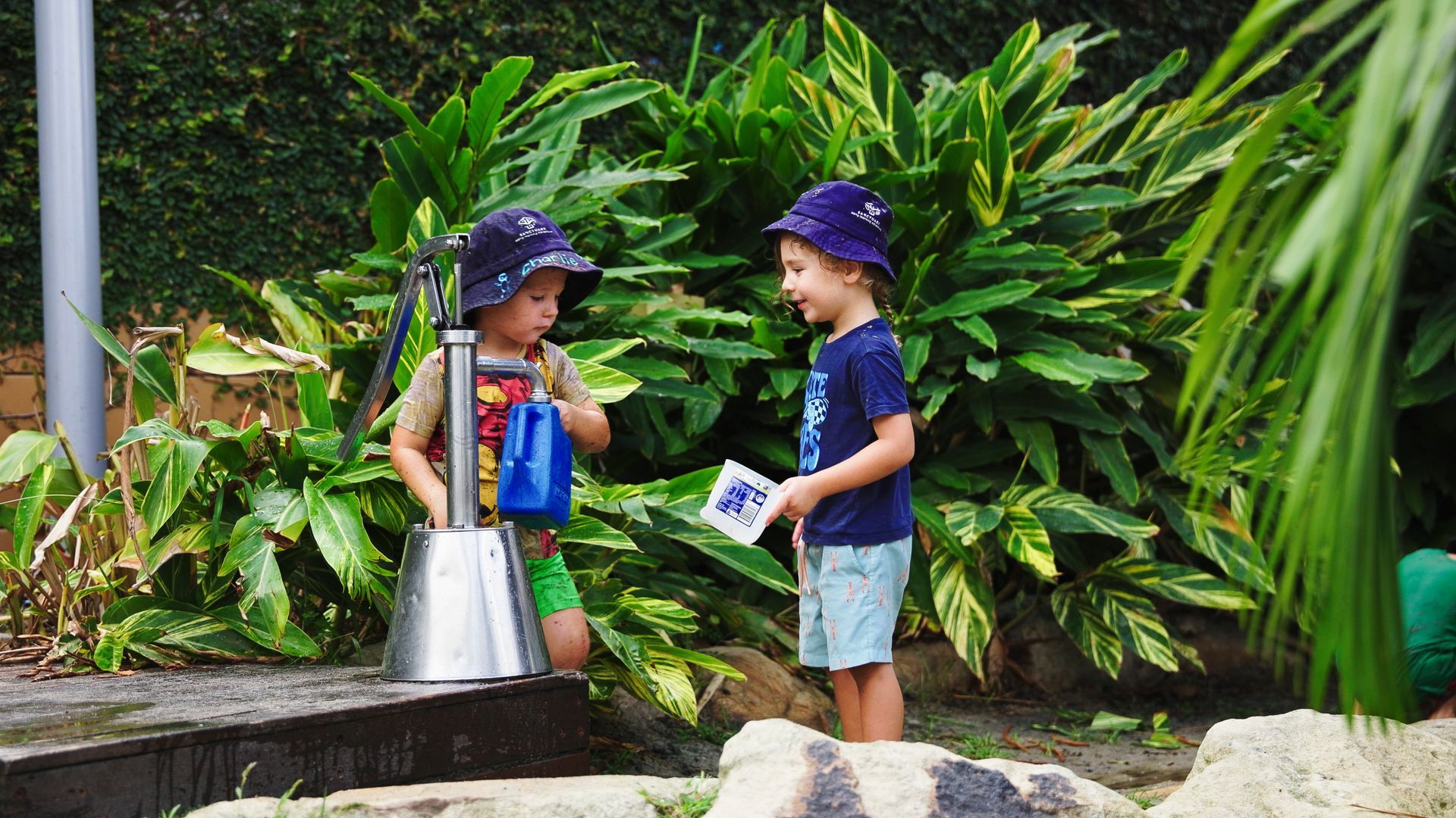 two children playing with water tap in yard outdoors
