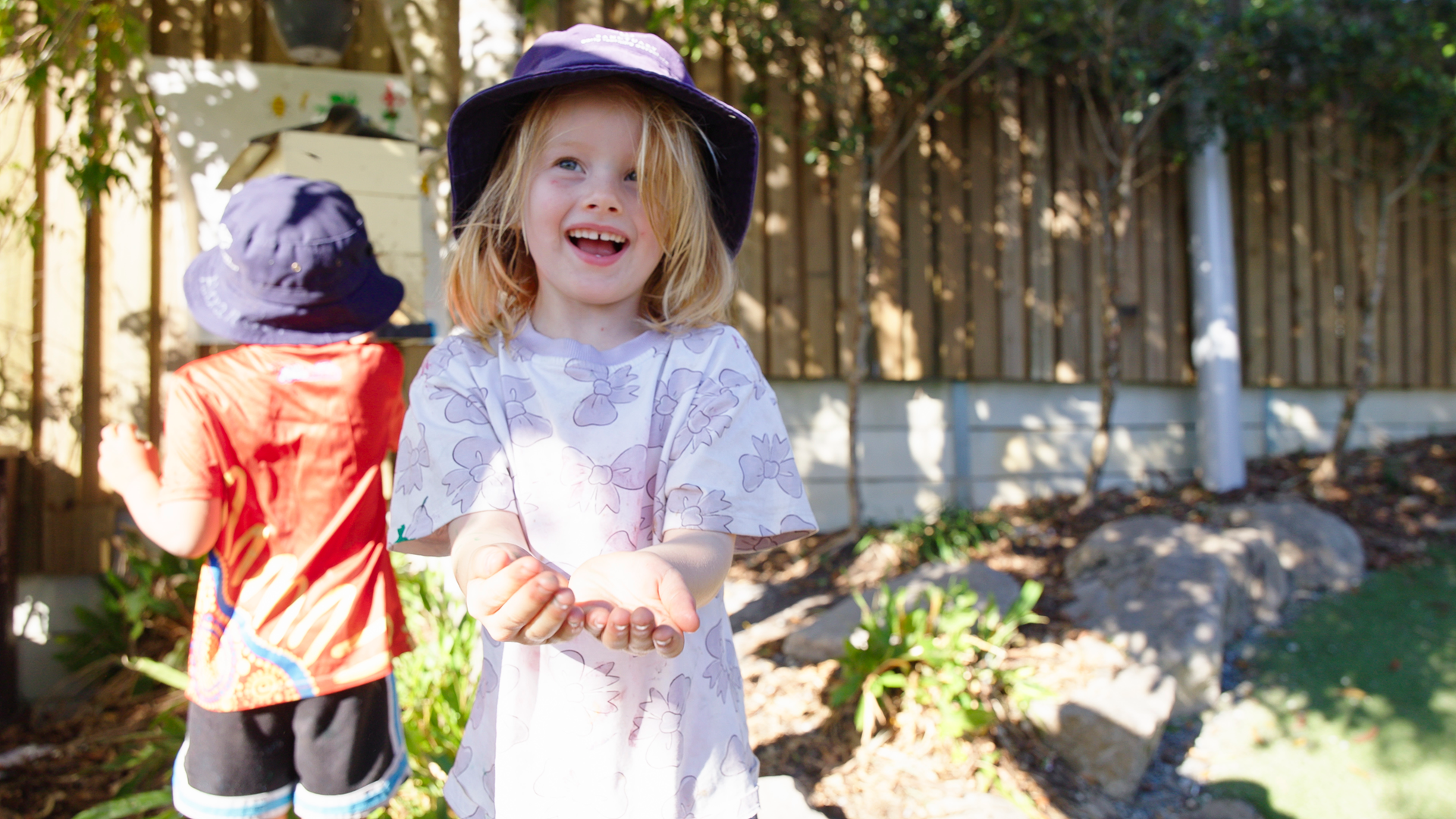 A child is happy, cupping her hands showing the camera she is holding something we cannot see.