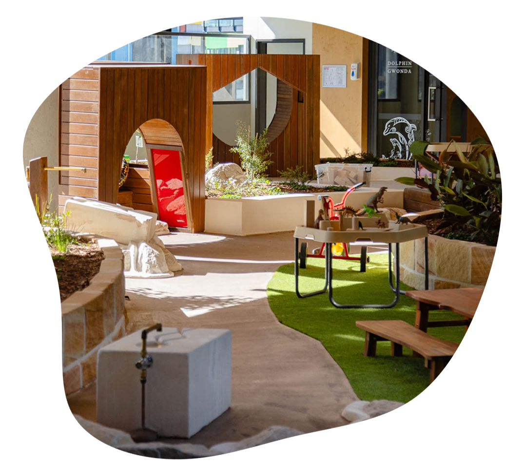 Outdoor playground with sandstone bricks, a winding path and wooden play spaces.