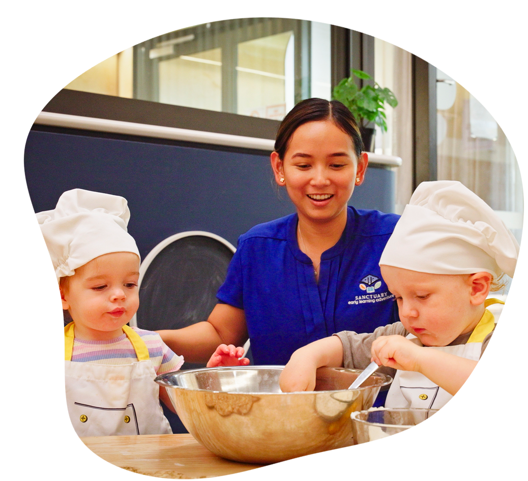 Two children in little chef outfits do some baking while an educator watches. 