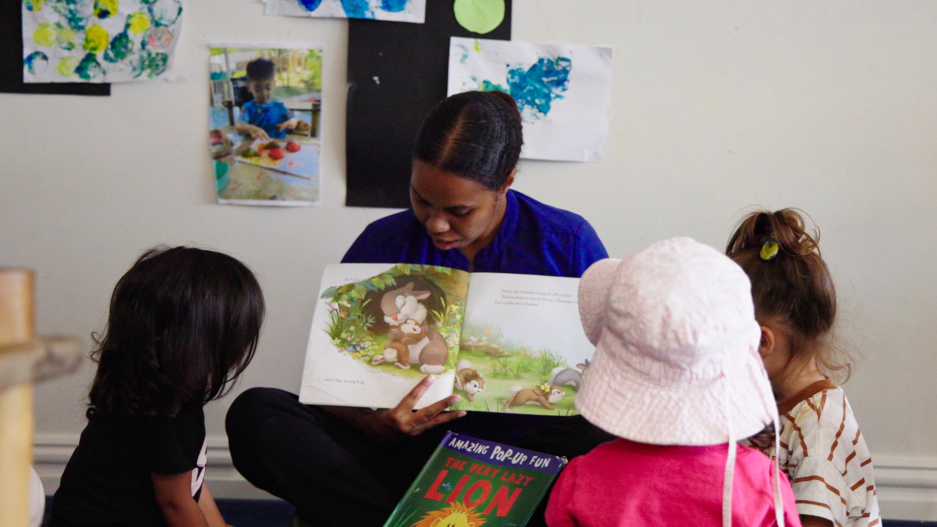 educator reads from an open book facing three children in an early learning setting