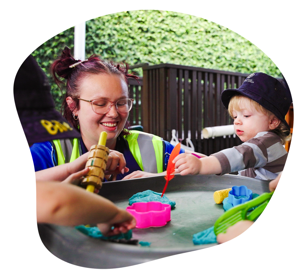 Children and adult building a tower with colorful blocks in a red container, outdoors.