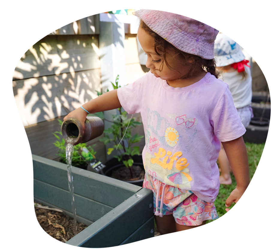 Child wearing hat outside watering garden