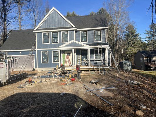 New house under construction, blue siding, white trim, with tools and materials scattered in the yard.