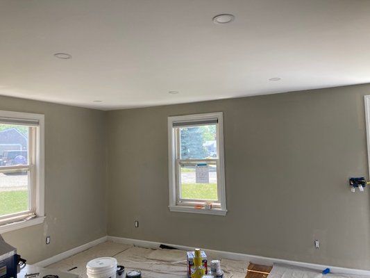 Empty room with olive-green walls, white ceiling, two windows, and recessed lighting.