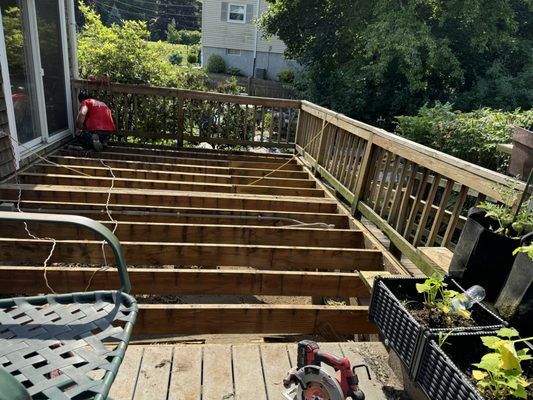 Deck under construction, missing boards, railings, person in red shirt working.