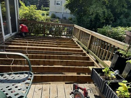 Deck under construction; worker in red shirt, removed decking, wooden railings, outdoor setting.