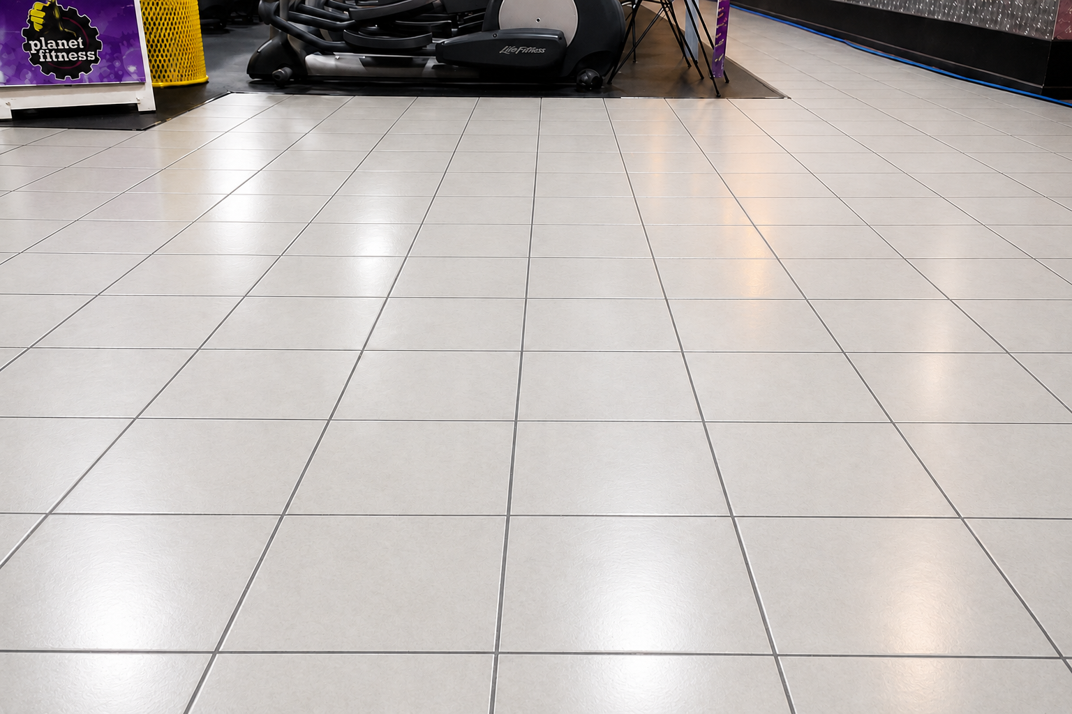 White tiled floor in a store aisle with shelves and a black stroller in the background