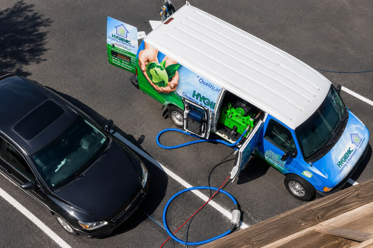 Blue and white service truck washing a black car with a hose in a parking lot