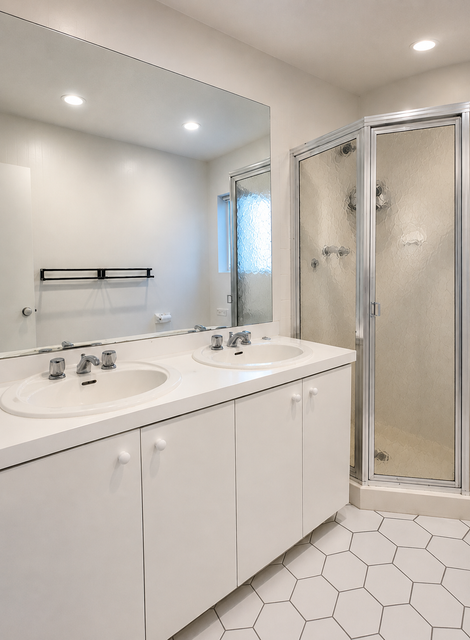 Bright modern bathroom with double vanity, large mirror, glass shower, and white hexagon tile floor