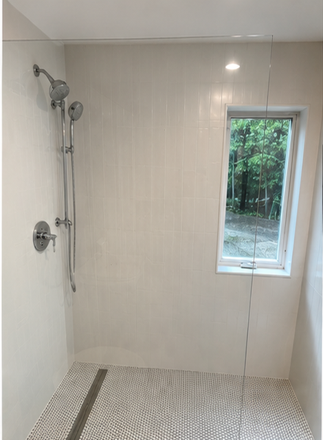 Empty tiled shower with handheld showerhead and a small window showing greenery outside