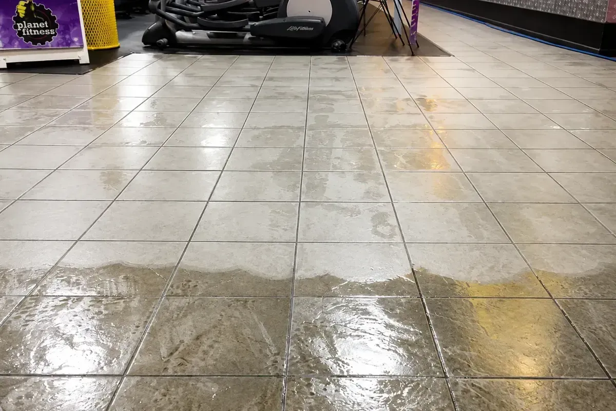 Wet tiled floor in a car wash bay, reflecting overhead lights.