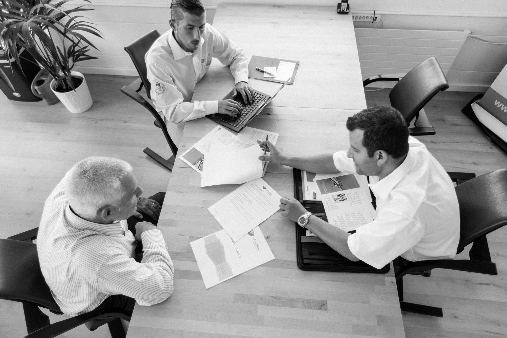 Vier Kolleginnen und Kollegen sitzen bei einem Büromeeting um einen Tisch mit Unterlagen und Laptops
