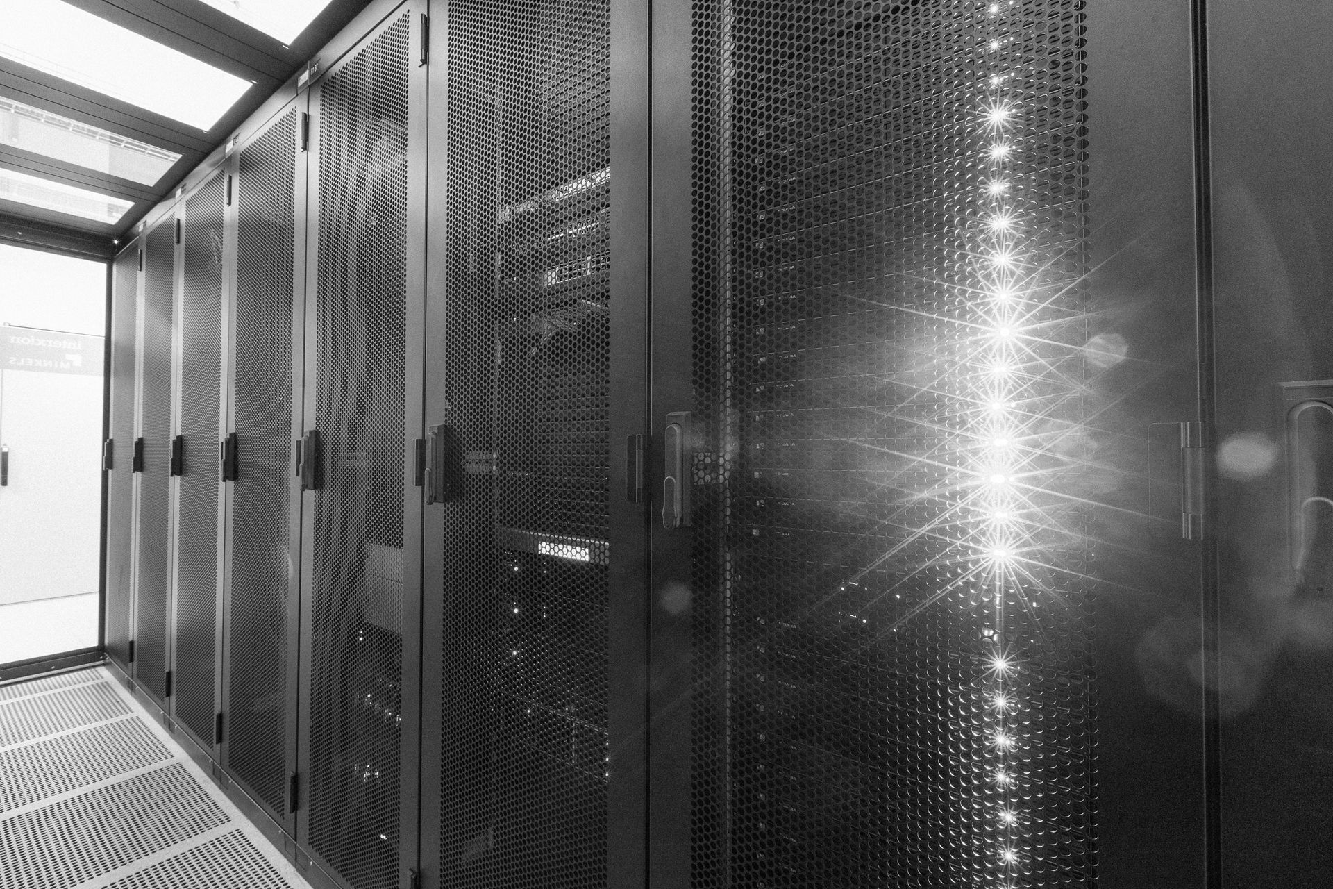Serverraumgang mit Reihen schwarzer Datenschränke und hellem Licht, das sich in den perforierten Türen spiegelt