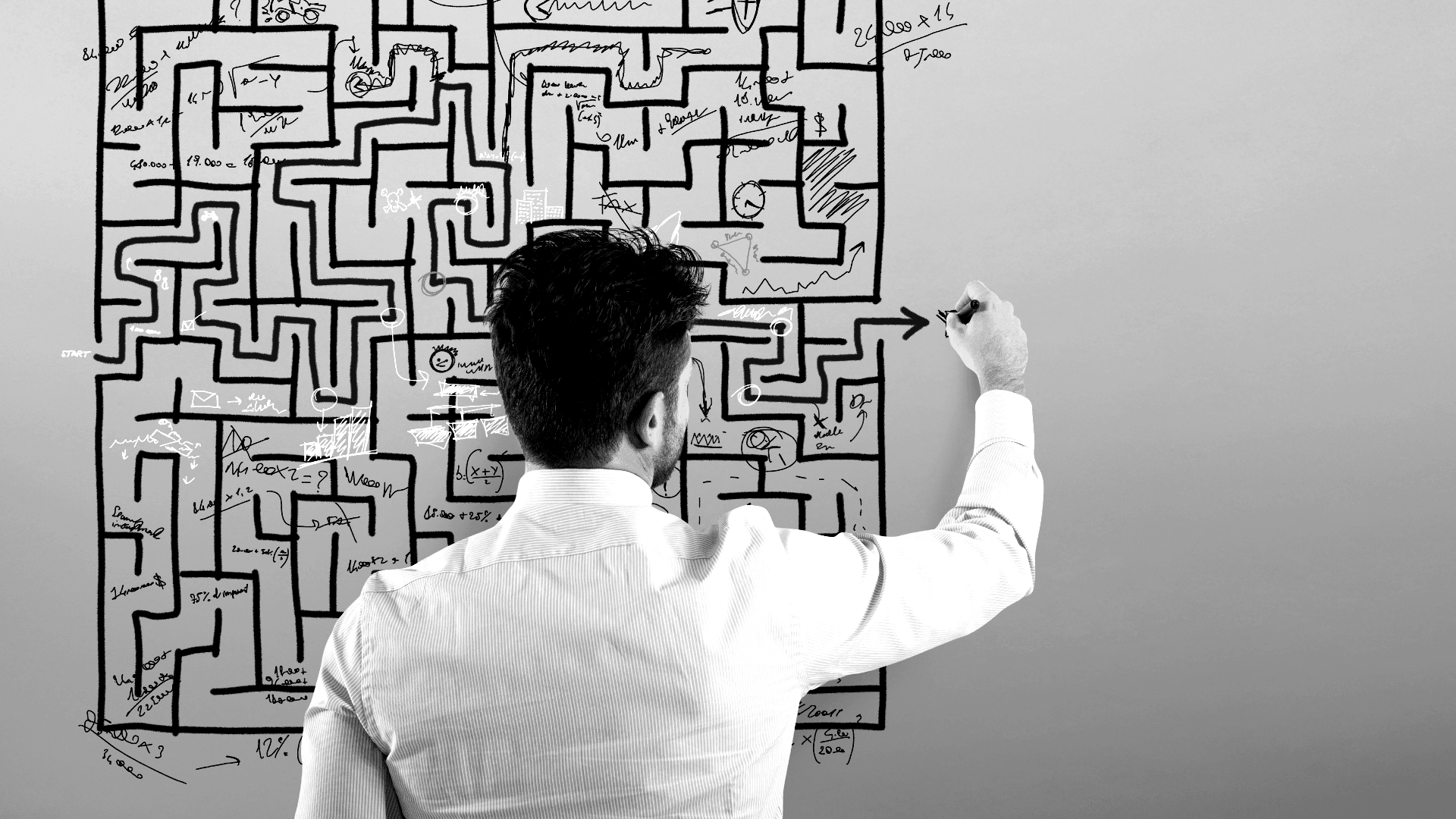 Person, die ein labyrinthartiges Muster aus miteinander verbundenen schwarzen Linien und Quadraten an eine Wand zeichnet