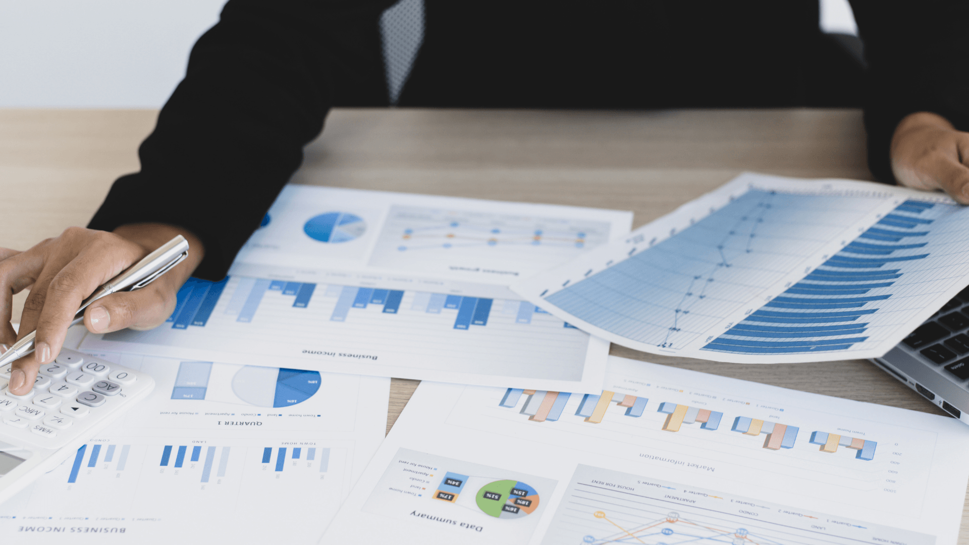 Eine Person betrachtet Finanzdiagramme und -grafiken, die auf einem Schreibtisch ausgebreitet sind, und hält dabei einen Stift und Papiere in der Hand.