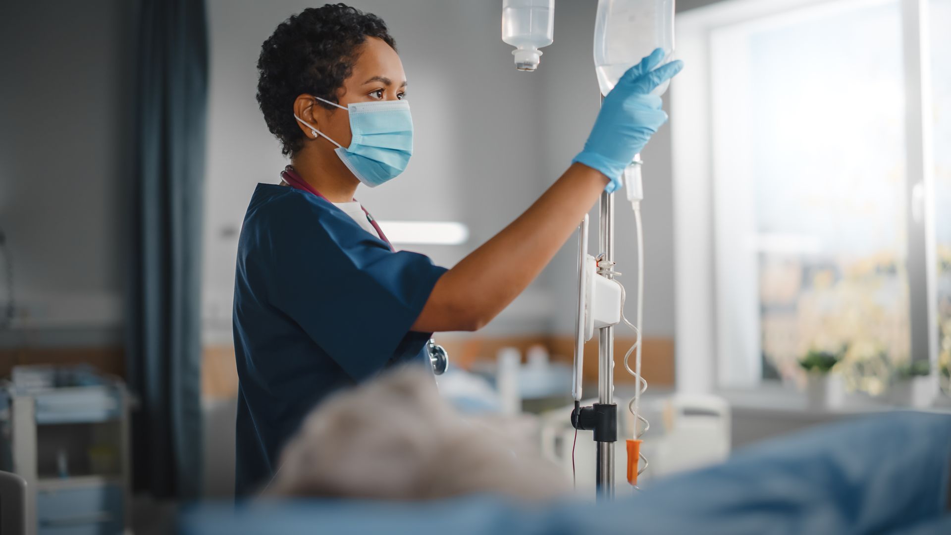 Professional Black Head Nurse Wearing Face Mask Does Checkup of Patient's Vitals. Caring Nurse Monitors Person Recovery.