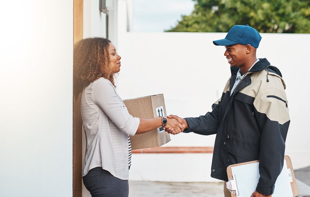 A delivery man is shaking hands with a woman who is holding a package.
