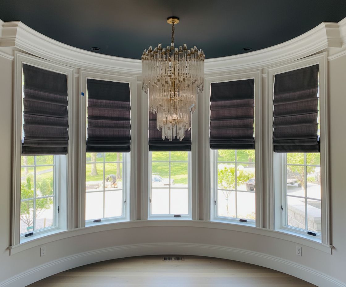 Bay window with grey roman shades and a crystal chandelier.