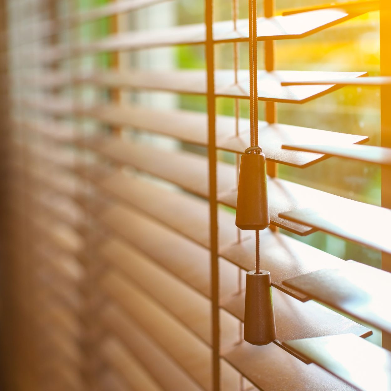 Close-up of brown wooden blinds with sunlight streaming through, showing the tilt mechanism.