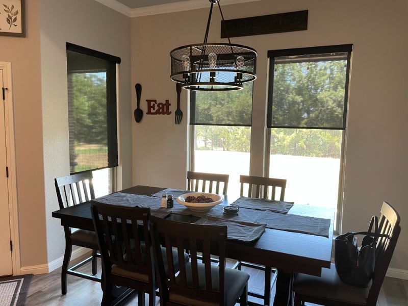 A dining room has three windows with brown motorized shades.