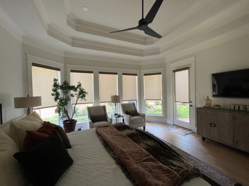 A bedroom with a bowed window has solar shades on each window section.