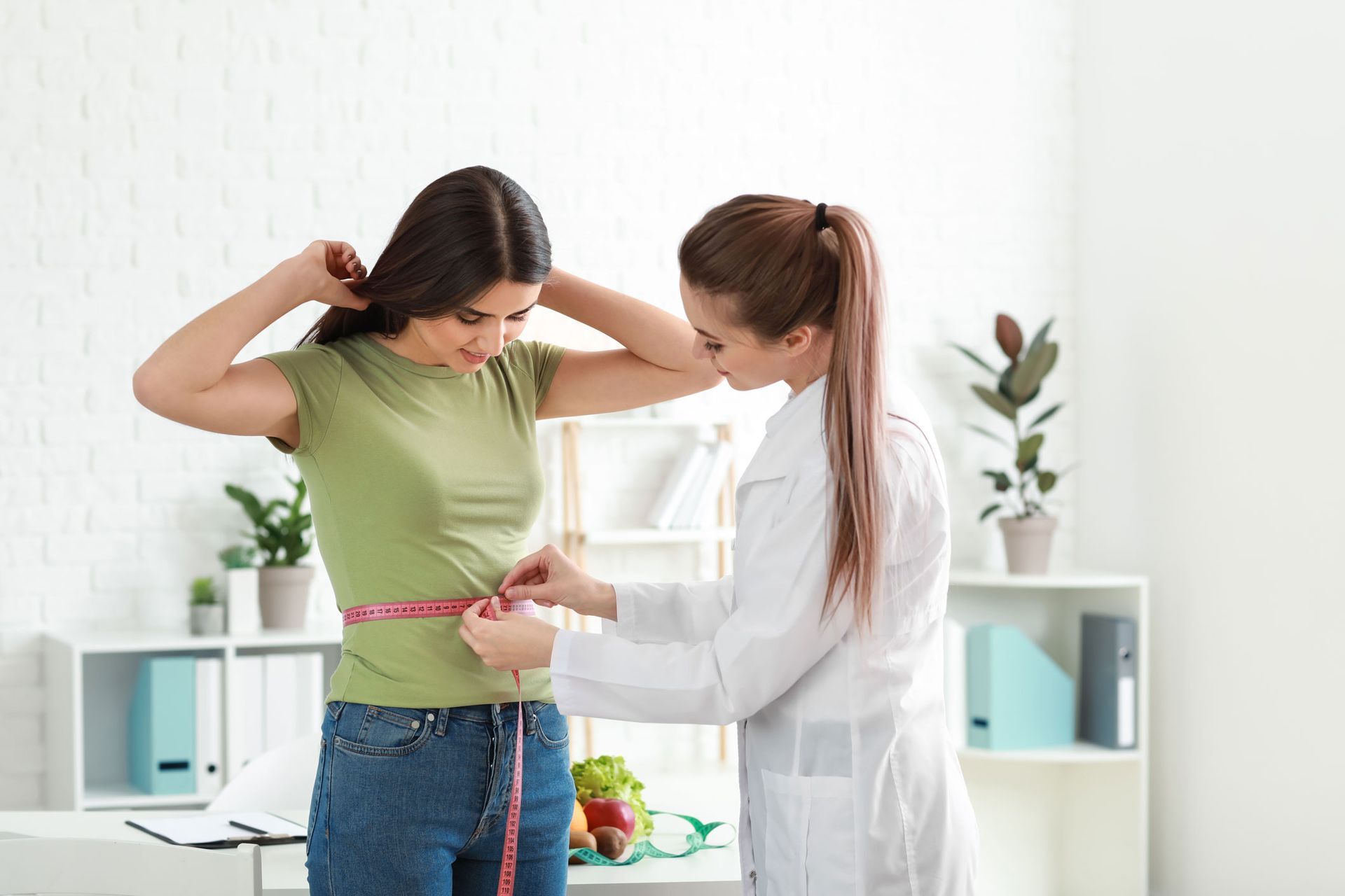 A female doctor measures the waist of a female patient inside a clinic.