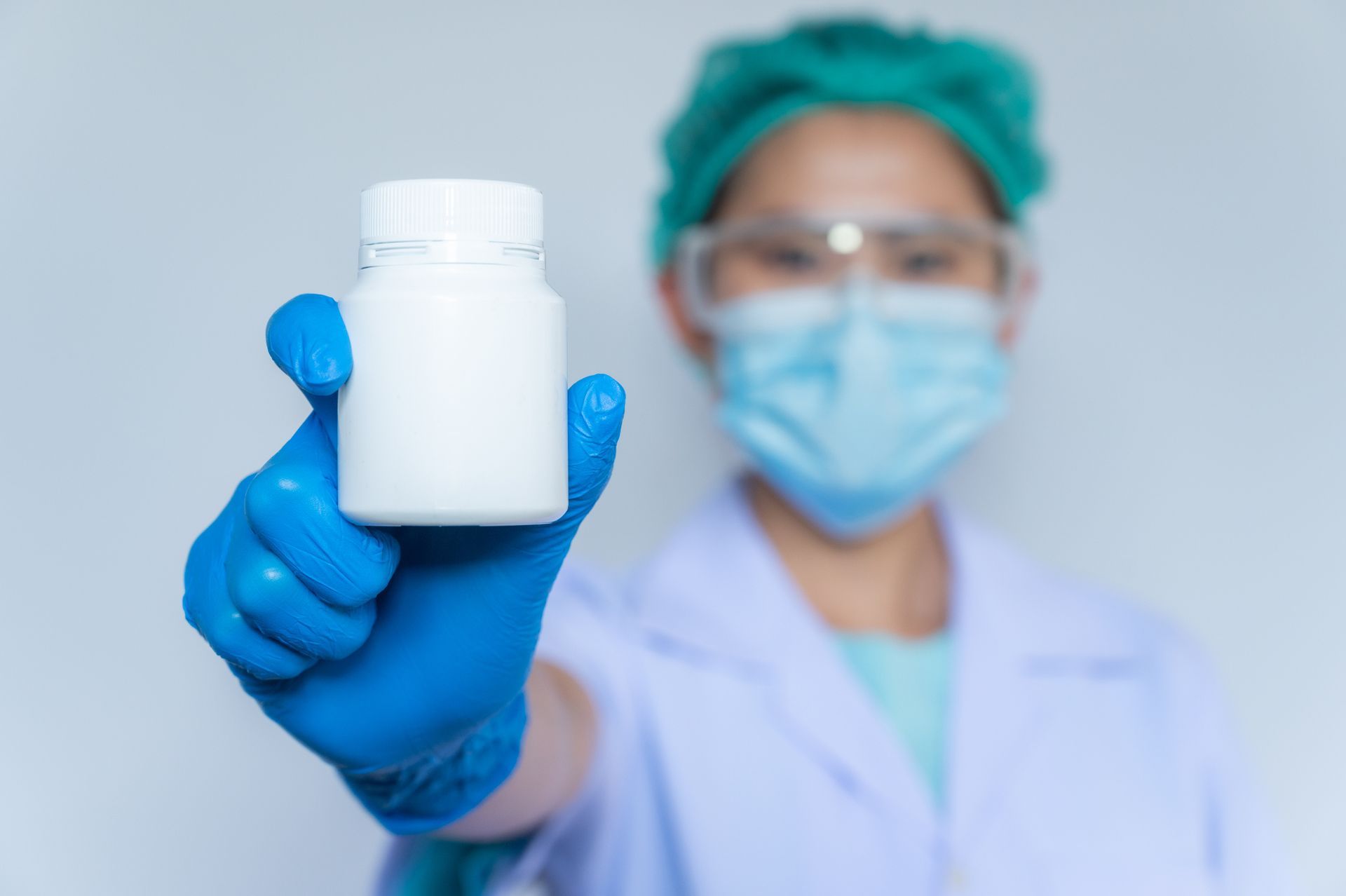 Person in PPE holding a white pill bottle, indicating medication.