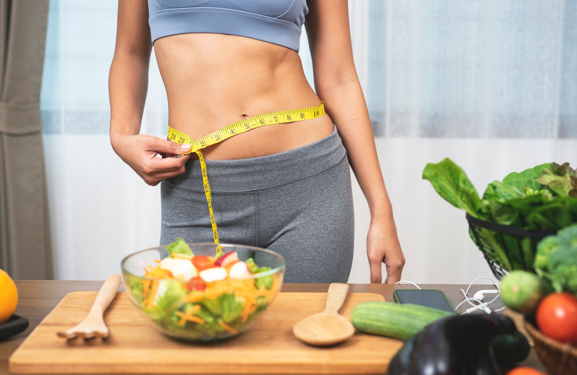 Woman measuring waist, near salad and vegetables, representing healthy eating.