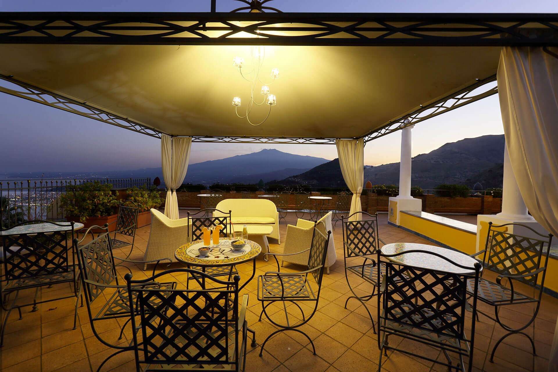 Eine Terrasse mit Tischen und Stühlen unter einem Baldachin mit Bergen im Hintergrund