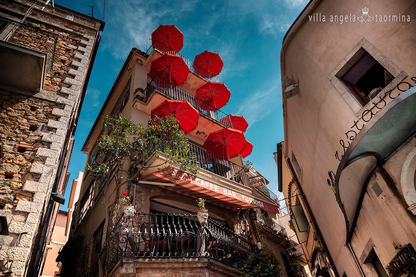 Blick nach oben auf ein Gebäude mit roten Regenschirmen auf dem Balkon