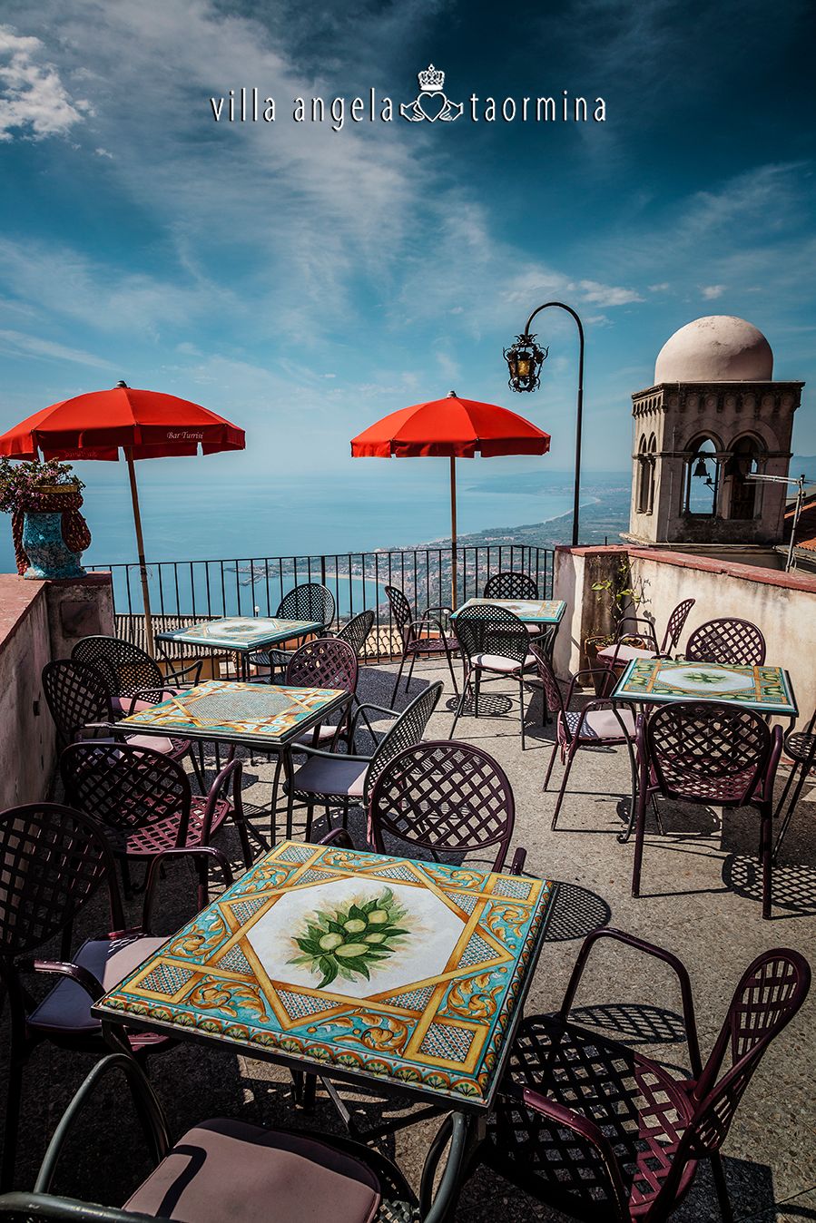 Eine Terrasse mit Tischen und Stühlen und roten Sonnenschirmen mit Blick auf den Ozean.