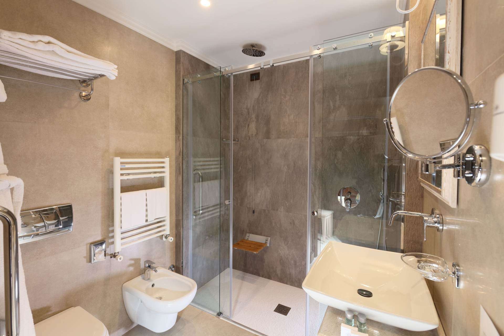 Ein Badezimmer mit Toilette, Waschbecken, Spiegel und ebenerdiger Dusche.