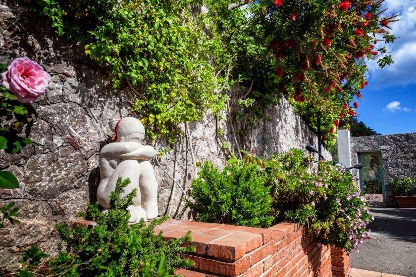 Eine Statue eines Mannes, der auf einer Backsteinmauer in einem Garten sitzt.