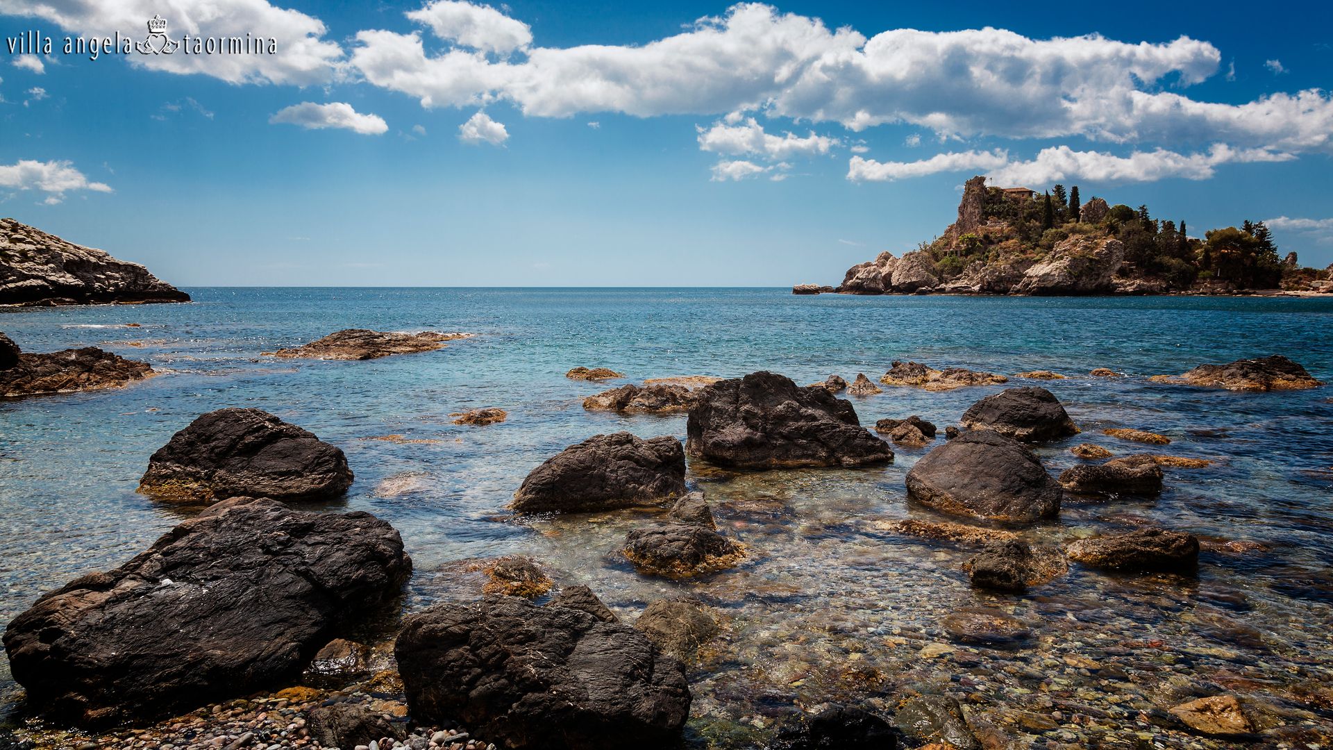 Ein großes Gewässer mit Felsen im Vordergrund und einer kleinen Insel im Hintergrund.