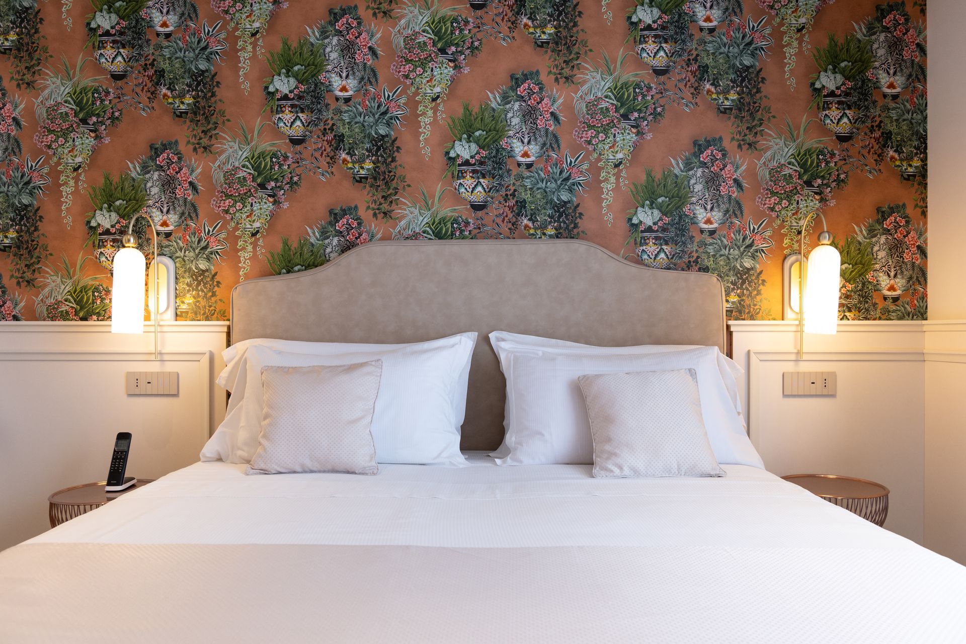 Ein Bett mit weißen Laken und Kissen in einem Hotelzimmer mit einer Blumentapete an der Wand.