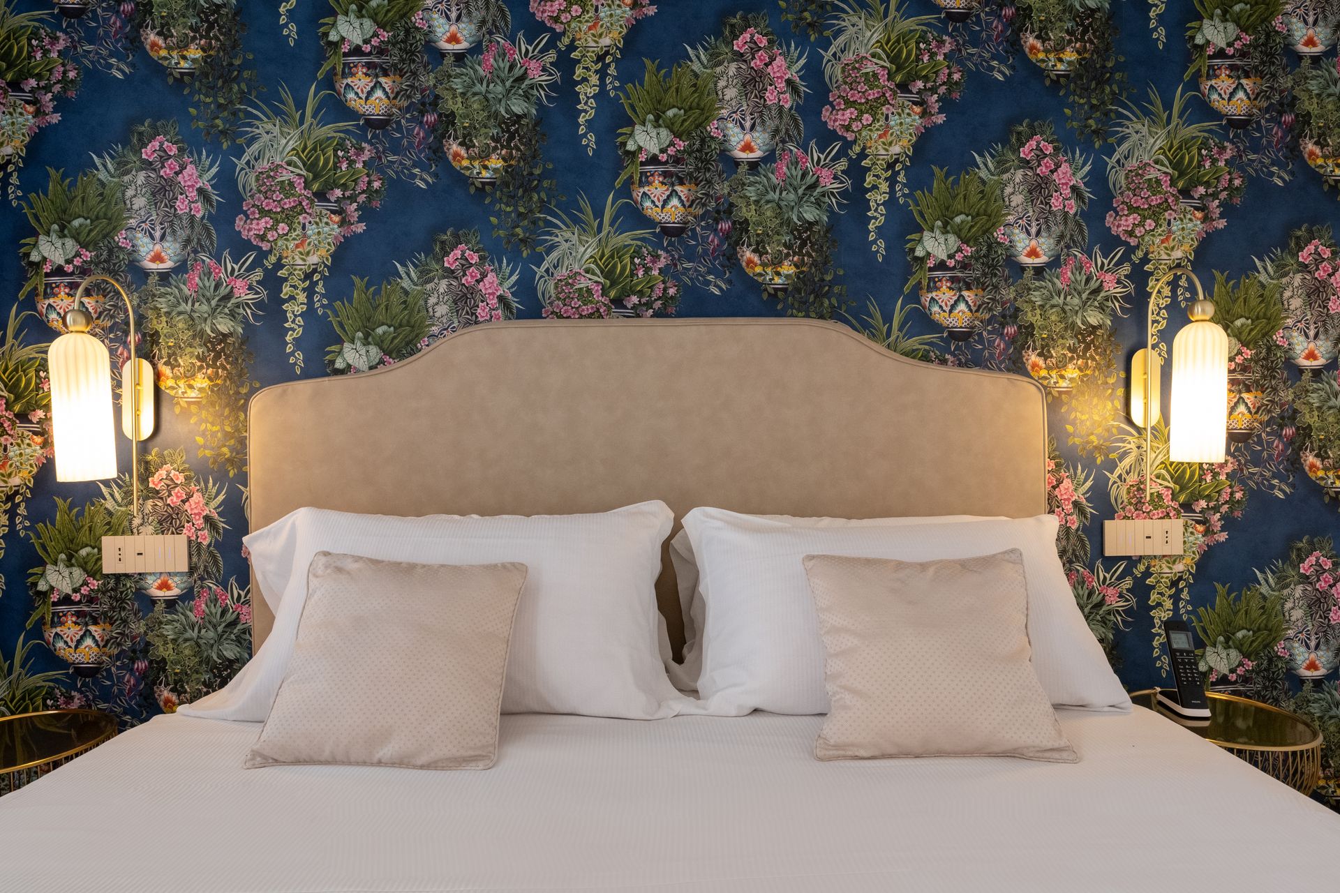 Ein Bett mit Kopfteil und Kissen in einem Hotelzimmer mit geblümter Tapete.