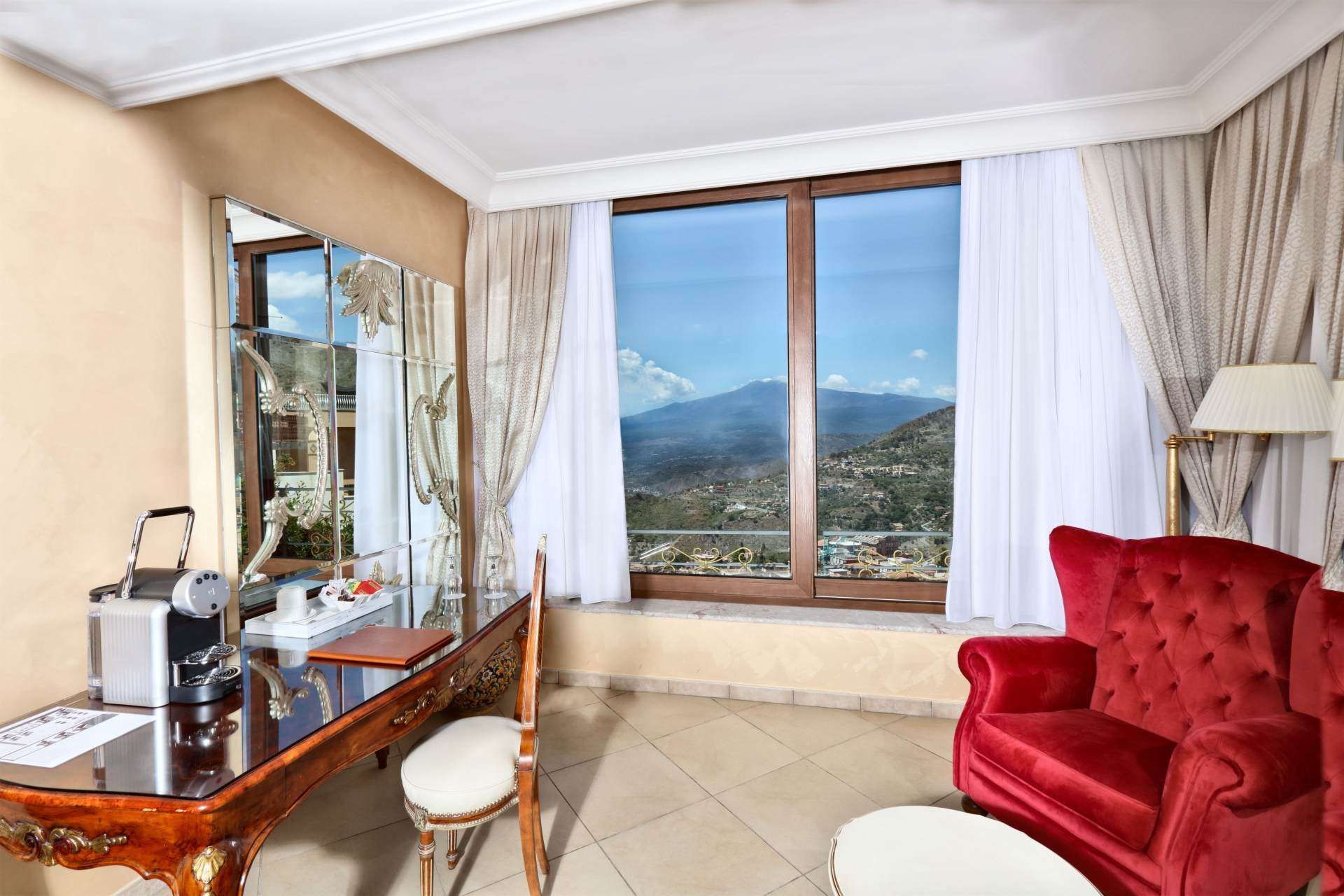 Ein Wohnzimmer mit Couch, Sessel, Schreibtisch und großem Fenster.