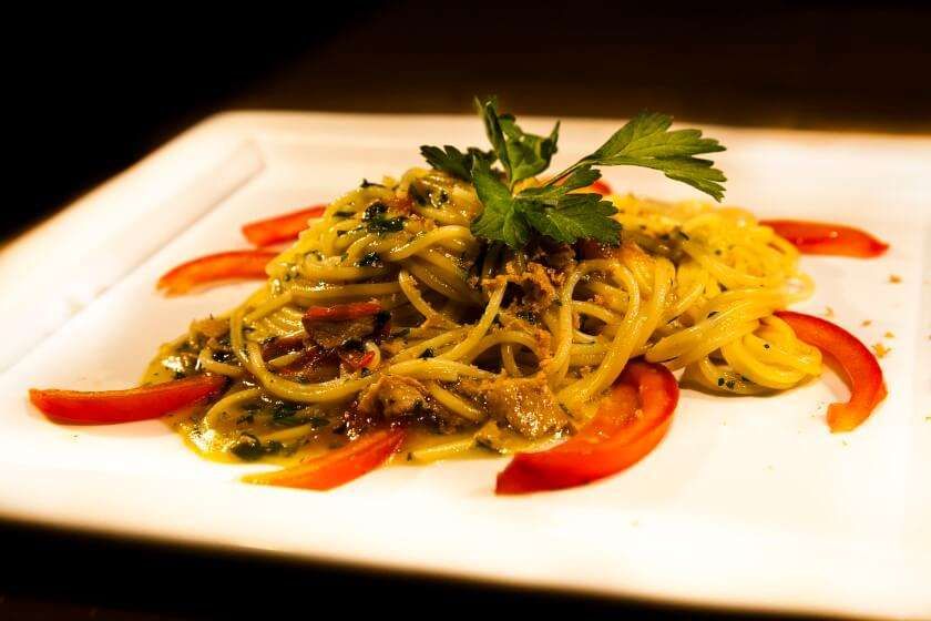 A white plate topped with spaghetti and tomatoes on a table.