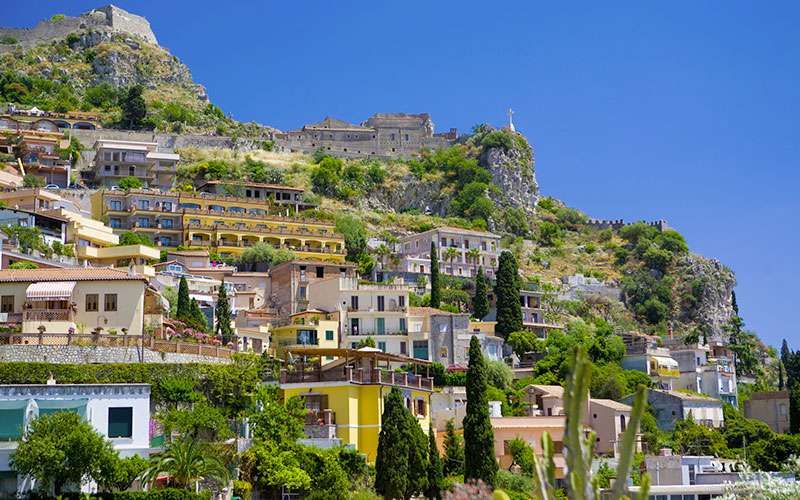 Eine kleine Stadt auf einem Hügel mit einer Burg im Hintergrund.