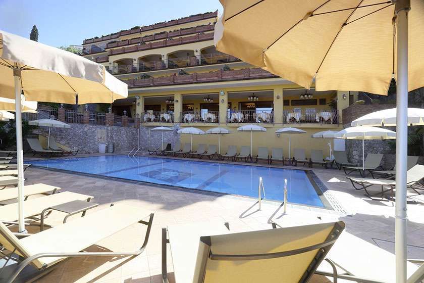 Ein großer Swimmingpool, umgeben von Stühlen und Sonnenschirmen vor einem Hotel.