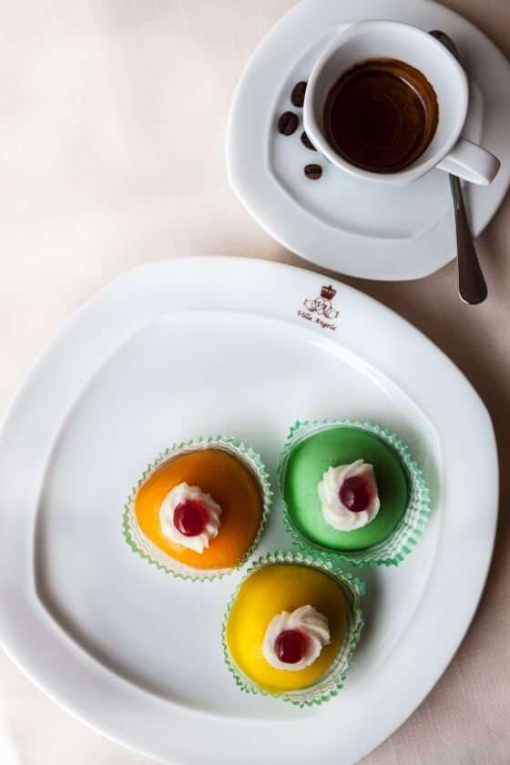 A white plate with three cupcakes on it next to a cup of coffee