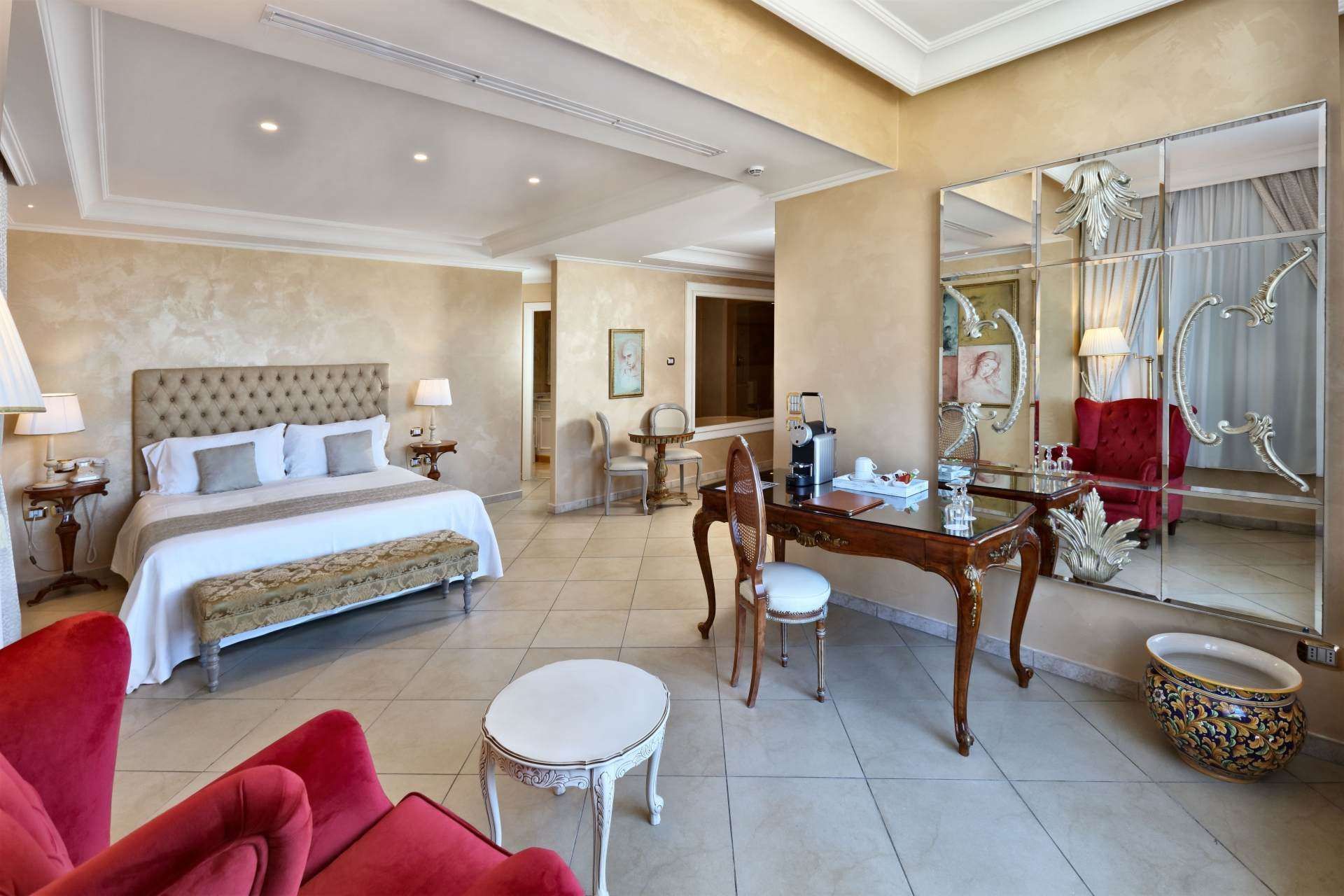 A hotel room with a king size bed , desk , chairs and a large mirror.